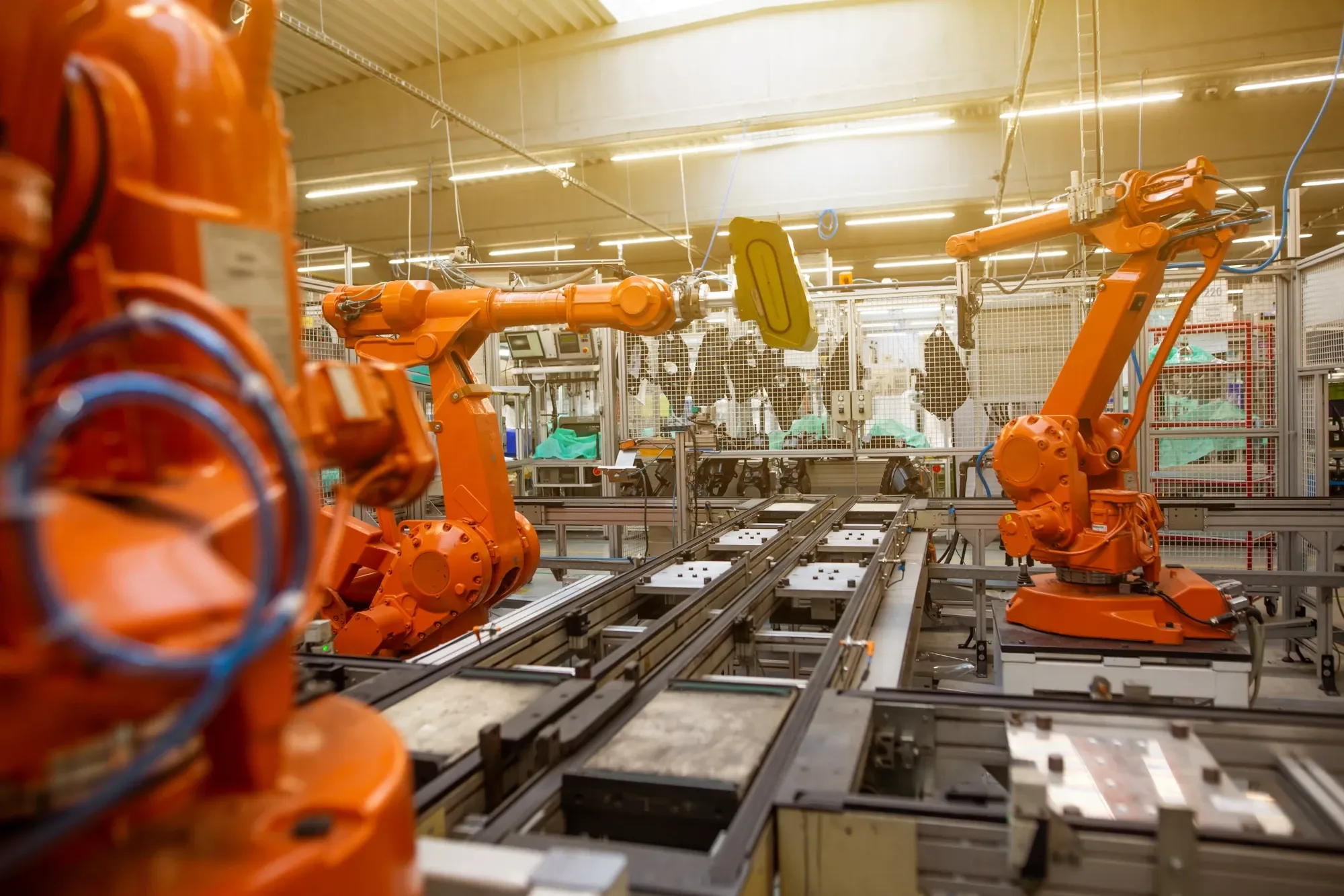 Orange industrial robot arms working on a conveyor line inside a factory